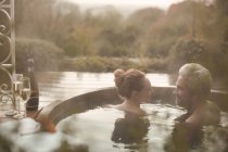 Couple talking soaking in hot tub with champagne on autumn patio — Stock Photo