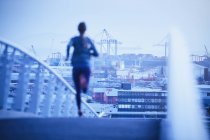 Läuferin läuft im Morgengrauen über städtische Fußgängerbrücke — Stockfoto