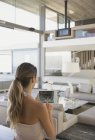 Frau mit digitalem Tablet stellt digitales Sicherheitssystem in modernem, luxuriösem Wohnzimmervitrine ein — Stockfoto