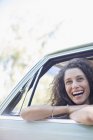 Щаслива красива жінка розслабляється на дверях автомобіля під час їзди на машині — стокове фото