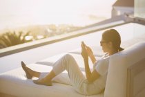 Woman using cell phone on chaise lounge at poolside on luxury patio — Stock Photo