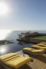 Sole splendente sulle sedie a sdraio a bordo piscina con vista sull'oceano — Foto stock
