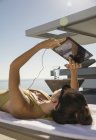 Donna prendere il sole, utilizzando tablet digitale sulla sedia a sdraio sul patio soleggiato — Foto stock