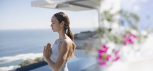 Heitere brünette Frau praktiziert Yoga, meditiert mit den Händen im Herzzentrum auf der sonnigen Terrasse mit Meerblick — Stockfoto