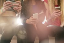 Teenage girls texting with cell phones in a row — Stock Photo