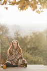 Mujer serena envuelta en manta meditando en patio de otoño - foto de stock