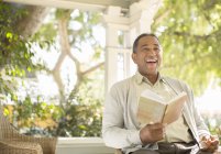 Laughing senior man reading book on porch — Stock Photo