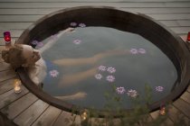 Mulher serena encharcada em banheira de hidromassagem com flores e velas no pátio — Fotografia de Stock