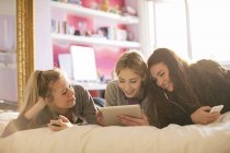 Teenage girls using cell phones and digital tablet on bed — Stock Photo