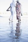 Vista trasera de las mujeres caminando descalzas en la playa - foto de stock