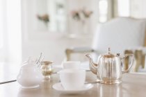 Tazas de té y tetera de plata en la mesa - foto de stock