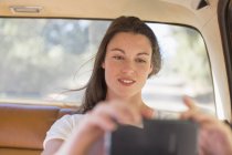 Mujer en coche tomando fotos con el teléfono celular - foto de stock