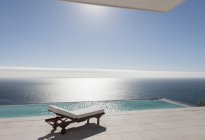 Chaise longue et piscine à débordement surplombant l'océan — Photo de stock