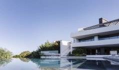 Tranquilo hogar escaparate interior con piscina infinita bajo el cielo azul soleado - foto de stock