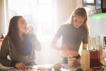 Teenage girls making smoothie in sunny kitchen — Stock Photo