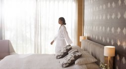 Mujer en albornoz caminando en el dormitorio - foto de stock