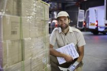 Portrait confident truck driver worker with scanner at pallet of cardboard boxes at distribution warehouse loading dock — Stock Photo