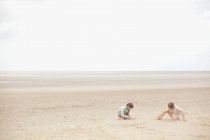 Irmão e irmã brincando na areia na praia nublada de verão — Fotografia de Stock