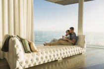 Cariñosa pareja bebiendo vino en un chaise lounge con vistas al mar - foto de stock