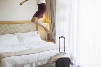 Businesswoman jumping on bed in hotel room — Stock Photo