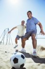 Старшие мужчины играют в футбол на пляже — стоковое фото