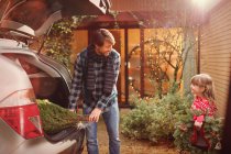 Father and daughter unloading Christmas tree from car outside house — Stock Photo