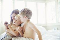 Children using cell phone on bed — Stock Photo