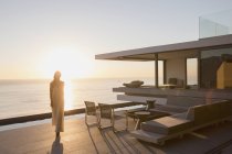 Женщина ходит по современной, роскошный дом витрина наружной палубе с видом на океан заката — стоковое фото