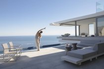 Frau praktiziert Yoga Side Stretch auf modernen, luxuriösen Haus Vitrine Außenterrasse mit sonnigem Meerblick — Stockfoto