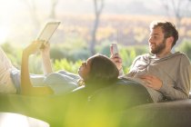 Couple pose et en utilisant tablette numérique et téléphone cellulaire sur terrasse ensoleillée — Photo de stock