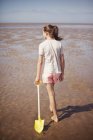 Adolescente menina arrastando pá na areia molhada na praia de verão ensolarada — Fotografia de Stock