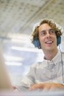 Happy young businessman listening to headphones in office — Stock Photo