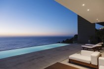 Terrasse moderne et piscine à débordement donnant sur l'océan au coucher du soleil — Photo de stock