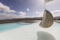 Pátio de luxo ensolarado e tranquilo com piscina infinita e assento suspenso com vista para o mar — Fotografia de Stock