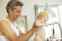 Батько миє дитину в кухонній мийці — стокове фото