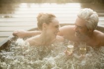 Улыбающаяся пара пьет шампанское, купаясь в джакузи на террасе — стоковое фото
