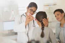 Médico femenino usando termómetro digital en oído de paciente niña en sala de examen - foto de stock