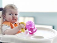 Baby girl playing with sippy cup in high chair — Stock Photo
