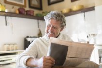 Older man reading news paper in kitchen — Stock Photo