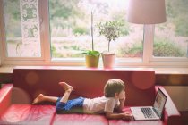 Мальчик использует ноутбук на красном кожаном диване в гостиной — стоковое фото