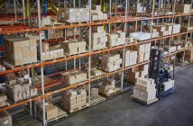 Carrello elevatore operante che muove scatole di cartone lungo gli scaffali del magazzino di distribuzione — Foto stock