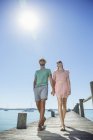 Couple holding hands walking along wooden dock — Stock Photo