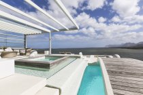 Sonniger, ruhiger, moderner Luxus-Innenhof mit Schwimmbad und Fußgängerbrücke mit Meerblick — Stockfoto