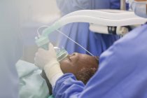 Primo piano del medico che indossa guanti chirurgici, che tiene la maschera di ossigeno sul paziente in sala operatoria — Foto stock