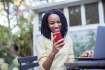 Smiling woman using cell phone and laptop on patio — Stock Photo