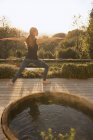 Woman practicing yoga warrior 2 pose on autumn patio with hot tub — Stock Photo