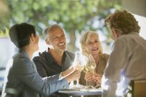Casais brindar copos de vinho branco na mesa de restaurante ensolarado — Fotografia de Stock
