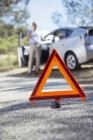 Man talking on cell phone at roadside behind warning triangle — Stock Photo
