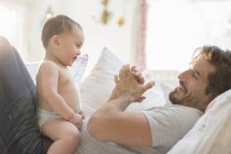 Cheerful father playing with baby son on sofa — Stock Photo