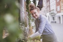 Portrait smiling young female florist arranging display at storefront — Stock Photo